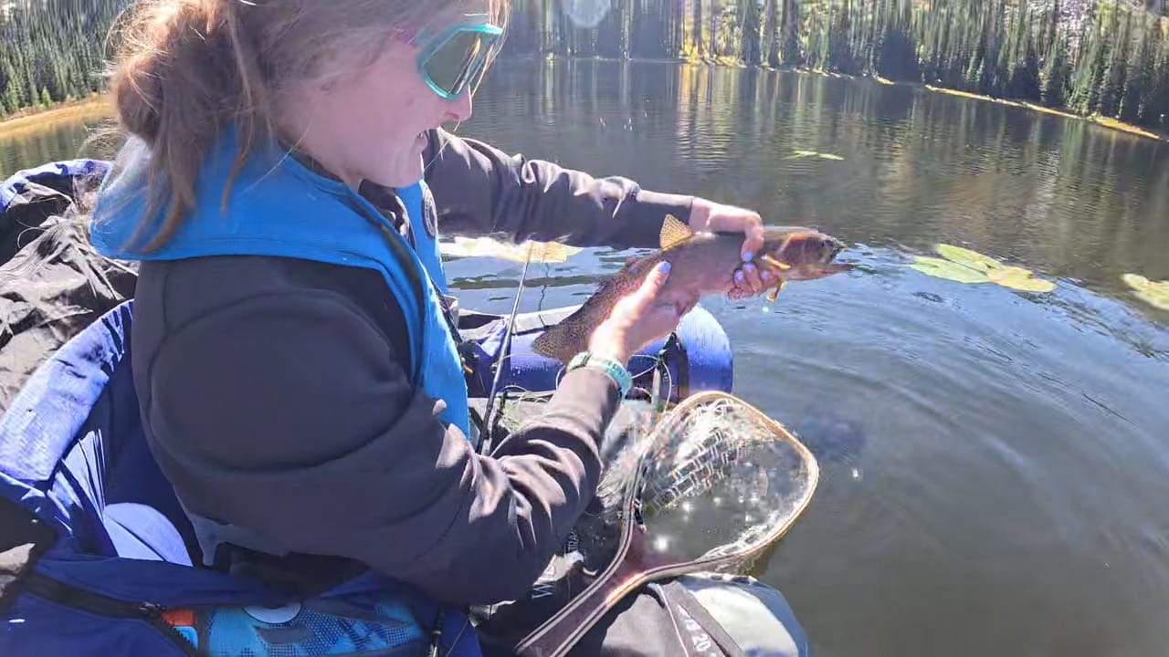 Picture of girl holding cutthroat fish up to the camera. Girl is on a float tube in a lake.