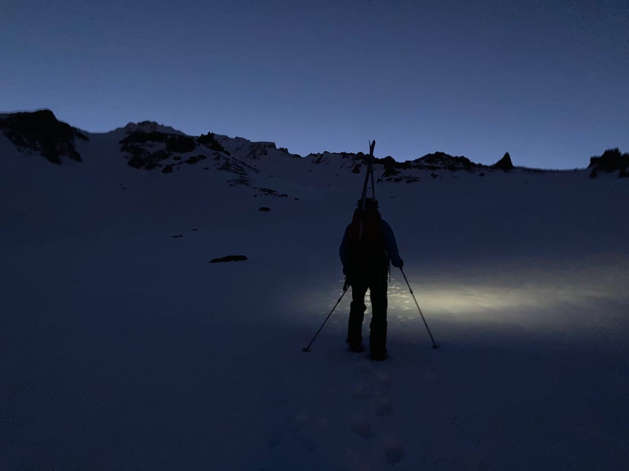 Pict of lone skier hiking mountain under glow of a headlamp.