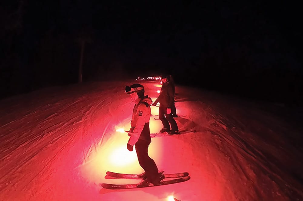 Picture of skiers holding road flares at start of torch light parade.