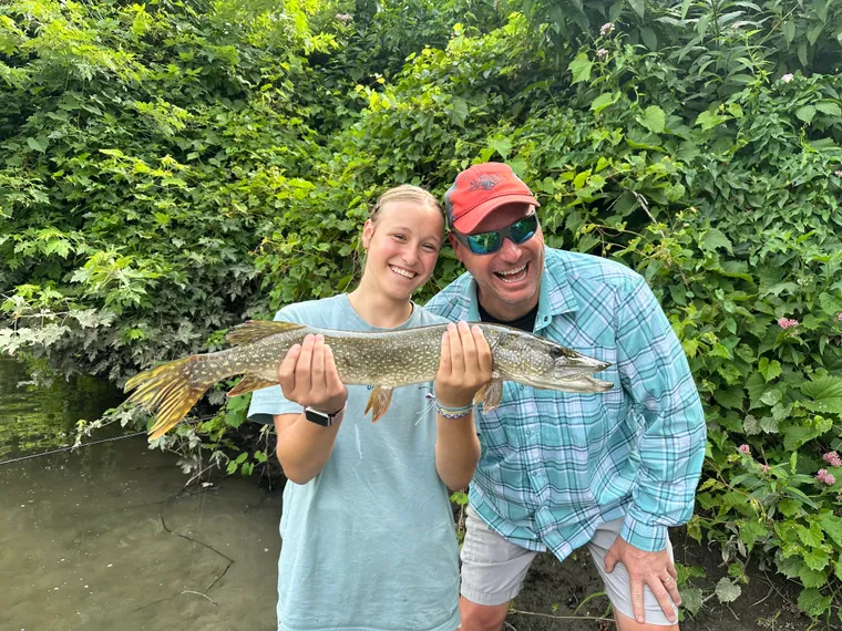 Picture of teenage girl holding a huge Pike. She's smiling next to her dad. 