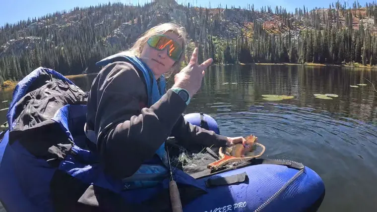 Picture of a woman giving the peace sign, while showing of the fish she just caught.